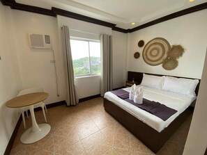A hotel room with a bed, a small table, a chair, a window with curtains, and a decorative wall piece. - Oceana Bay Coron (Coron)
