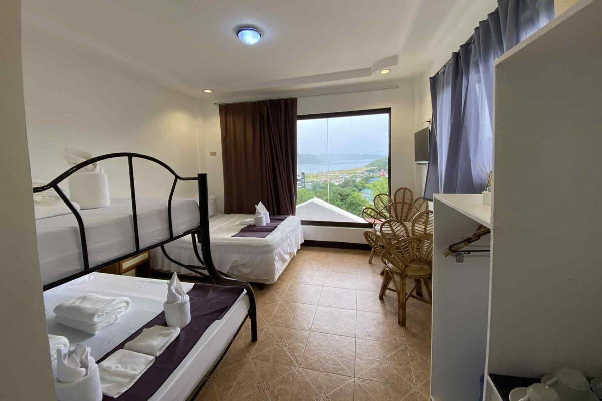 A hotel room with two beds, a view of the city, a dining area with chairs, and a TV on the wall.