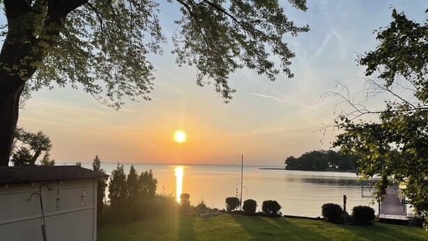 A grassy area with a wooden deck and picnic table, overlooking a calm body of water with a sunset in the background. - Lake Winnebago Water Front! Fishing! Boating! Quiet Bay! EAA! (Oshkosh)