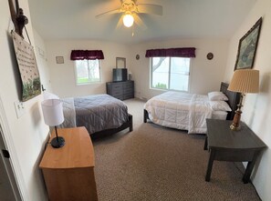 Ein Schlafzimmer mit zwei Betten, einem Deckenventilator, einem Schreibtisch, einer Lampe und einer Kommode.