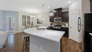 A modern kitchen with dark cabinets, stainless steel appliances, and a large island with a sink. - Where Relaxation Meets Home, KING Suite RETREAT, 14 MINS to RDU Airport, POOL (Morrisville)