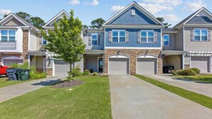 A two-story townhouse with a stone facade, a front garage, and a well-maintained lawn. - Where Relaxation Meets Home, KING Suite RETREAT, 14 MINS to RDU Airport, POOL (Morrisville)