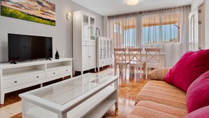 A modern living room with a flat-screen TV, white cabinets, a glass coffee table, a sofa, and a dining area with chairs and a table. - Micarlo 601 - Terrace, Second line of beach. 2 bedrooms (Torremolinos)