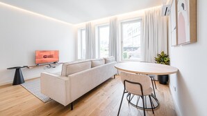 Un salon moderne comprenant un canapé, un téléviseur, une table à manger avec des chaises et de grandes fenêtres avec des rideaux.