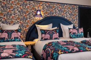 Une chambre d’hôtel avec un papier peint à motifs floraux, une tête de lit sombre et une literie à imprimé léopard.