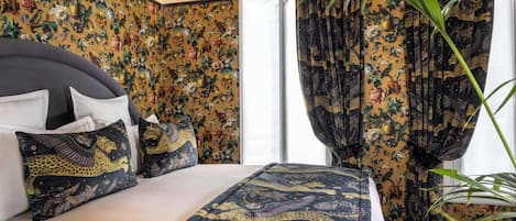 A hotel room with a bed, floral wallpaper, and curtains with a jungle theme.