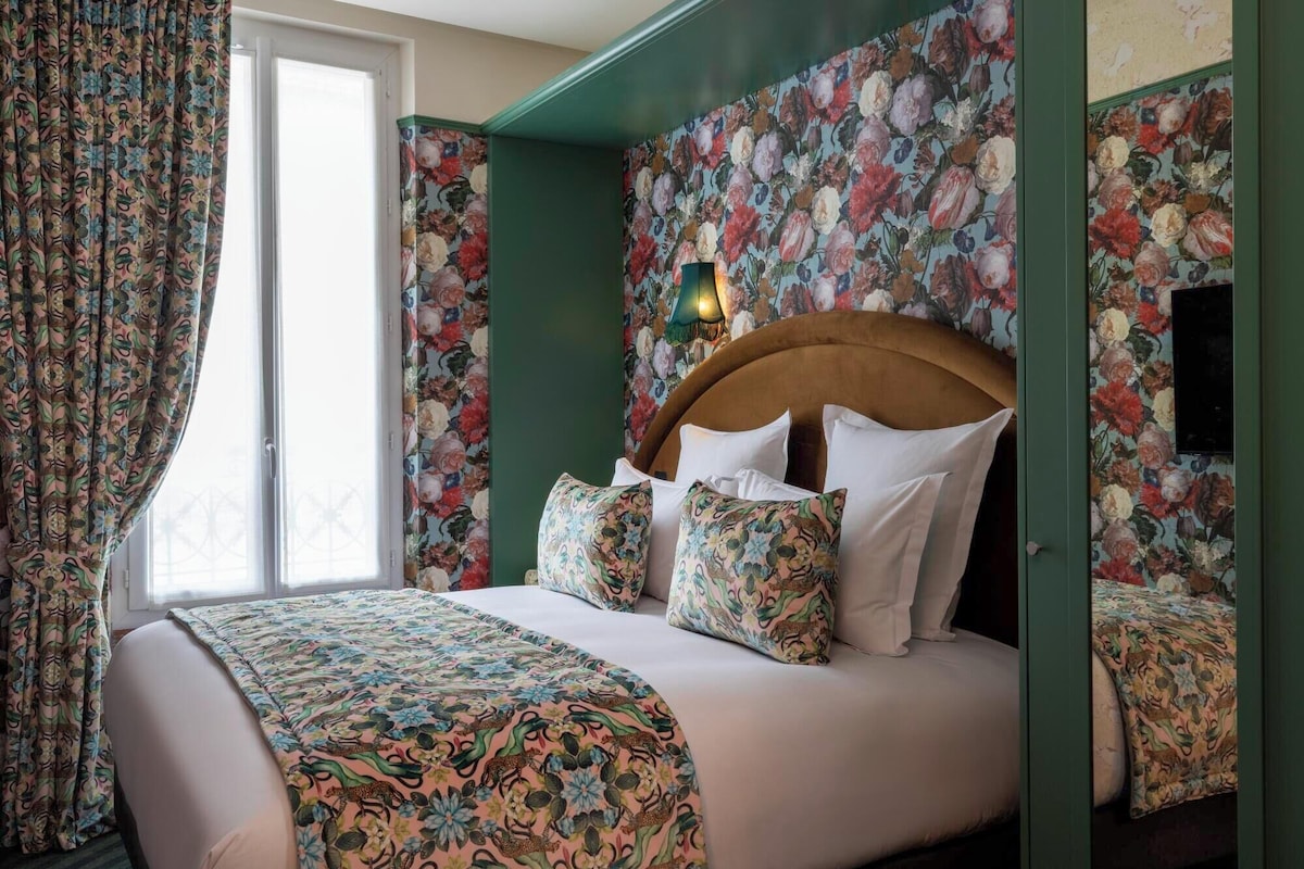 Un dormitorio con cubrecama estampado de flores, cortinas a juego y una pared verde decorativa.