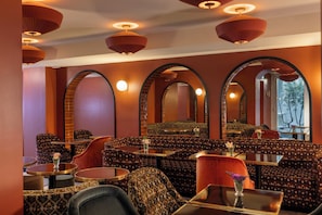 A restaurant with patterned seating, round tables, and arched mirrors.