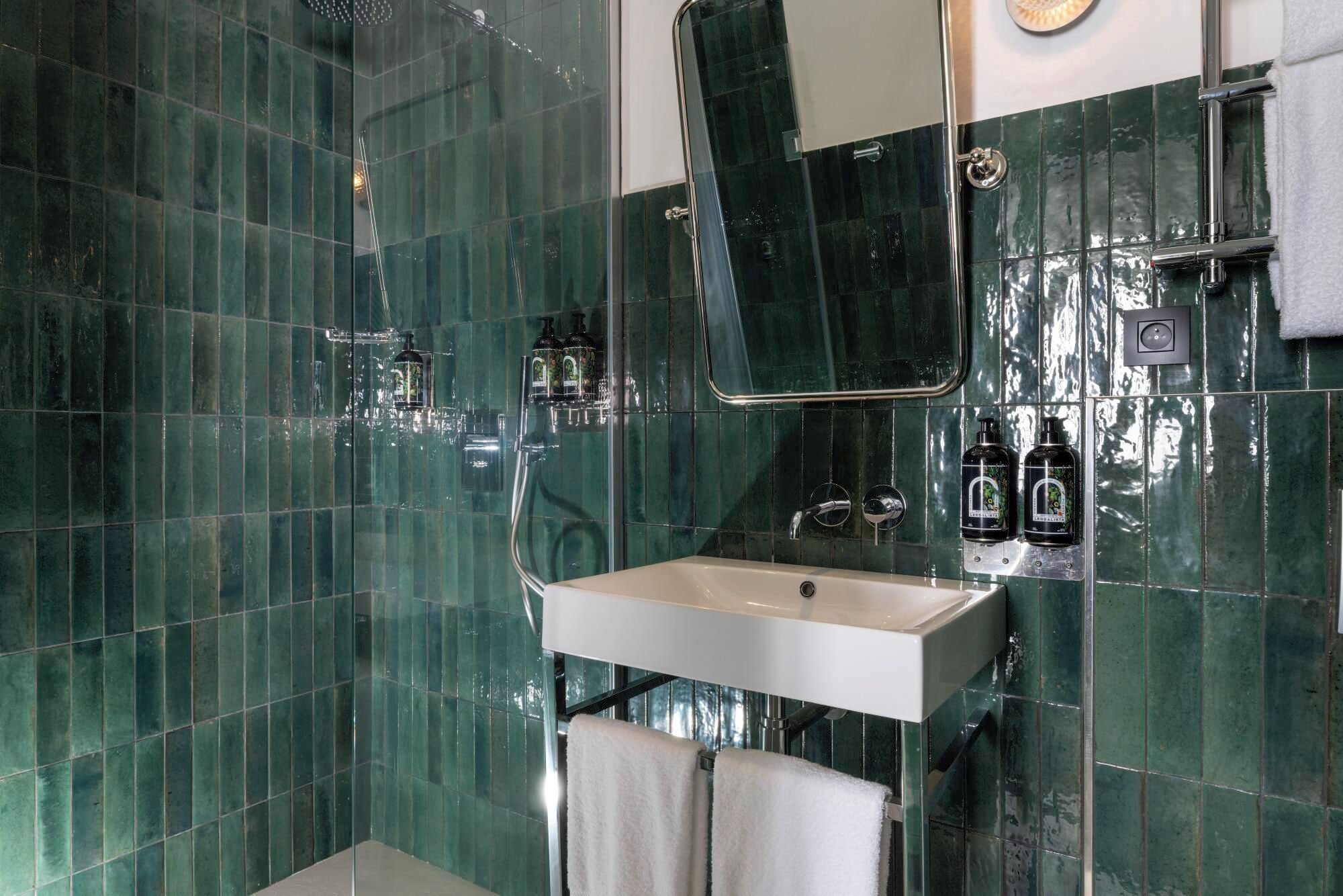 A bathroom with green tiles, a white sink, and two hand soap dispensers.