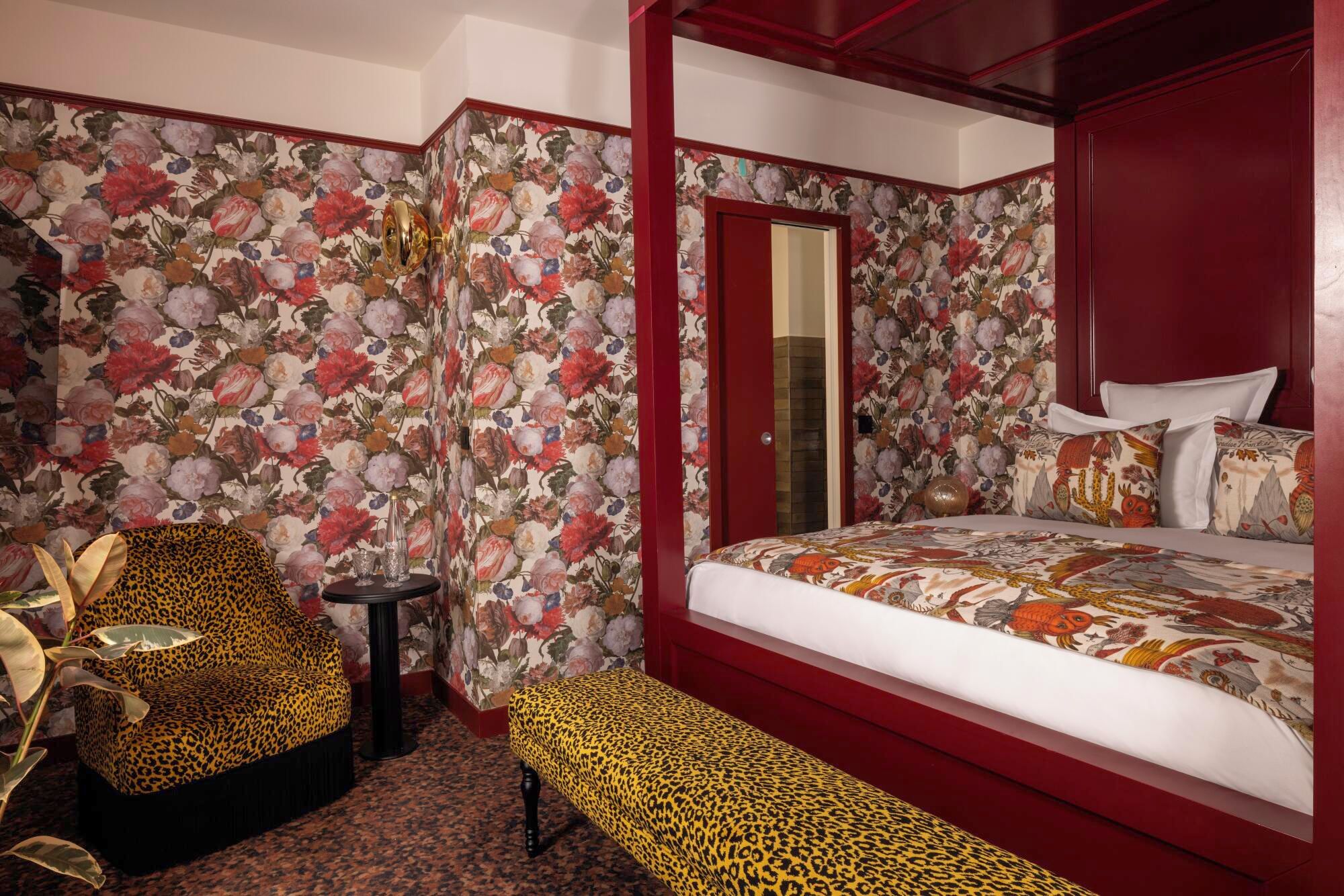 A bedroom with a four-poster bed, floral wallpaper, leopard print furniture, and a bench.