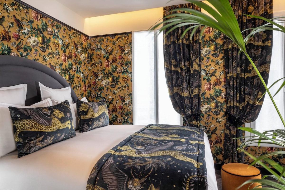 Una habitación de hotel con cama, papel tapiz floral y cortinas con temática selvática.