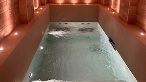 A spa room with a rectangular hot tub, arched brick walls, and recessed lighting.