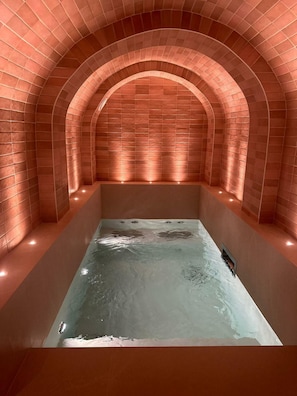 A spa room with a rectangular hot tub, arched brick walls, and recessed lighting.