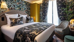 Camera d'albergo con un letto grande, carta da parati floreale, un armadio giallo, una poltrona a leopardata e un'ampia finestra con tende.