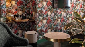 Una stanza con carta da parati a motivi floreali, una televisione a schermo piatto, un tavolo rotondo, una sedia e una mensola con oggetti decorativi.