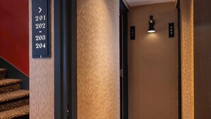 Un corridoio d'albergo con una scala, una targa fissata alla parete con i numeri delle camere e un punto luce a parete.