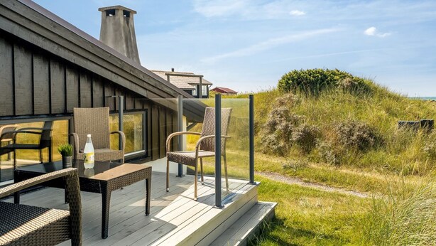 Een modern terras buiten met rieten meubilair en een glazen balustrade met uitzicht op een groene omgeving.