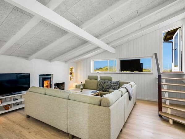 A spacious living room with a large sectional sofa, a flat-screen TV, a fireplace, and a wooden staircase.