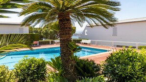Une piscine entourée d’une végétation luxuriante, avec un bâtiment blanc en arrière-plan.