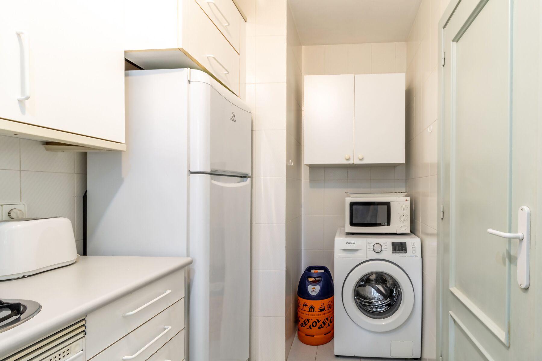 Une cuisine compacte équipée d’un réfrigérateur, d’un four à micro-ondes et d’un lave-linge.