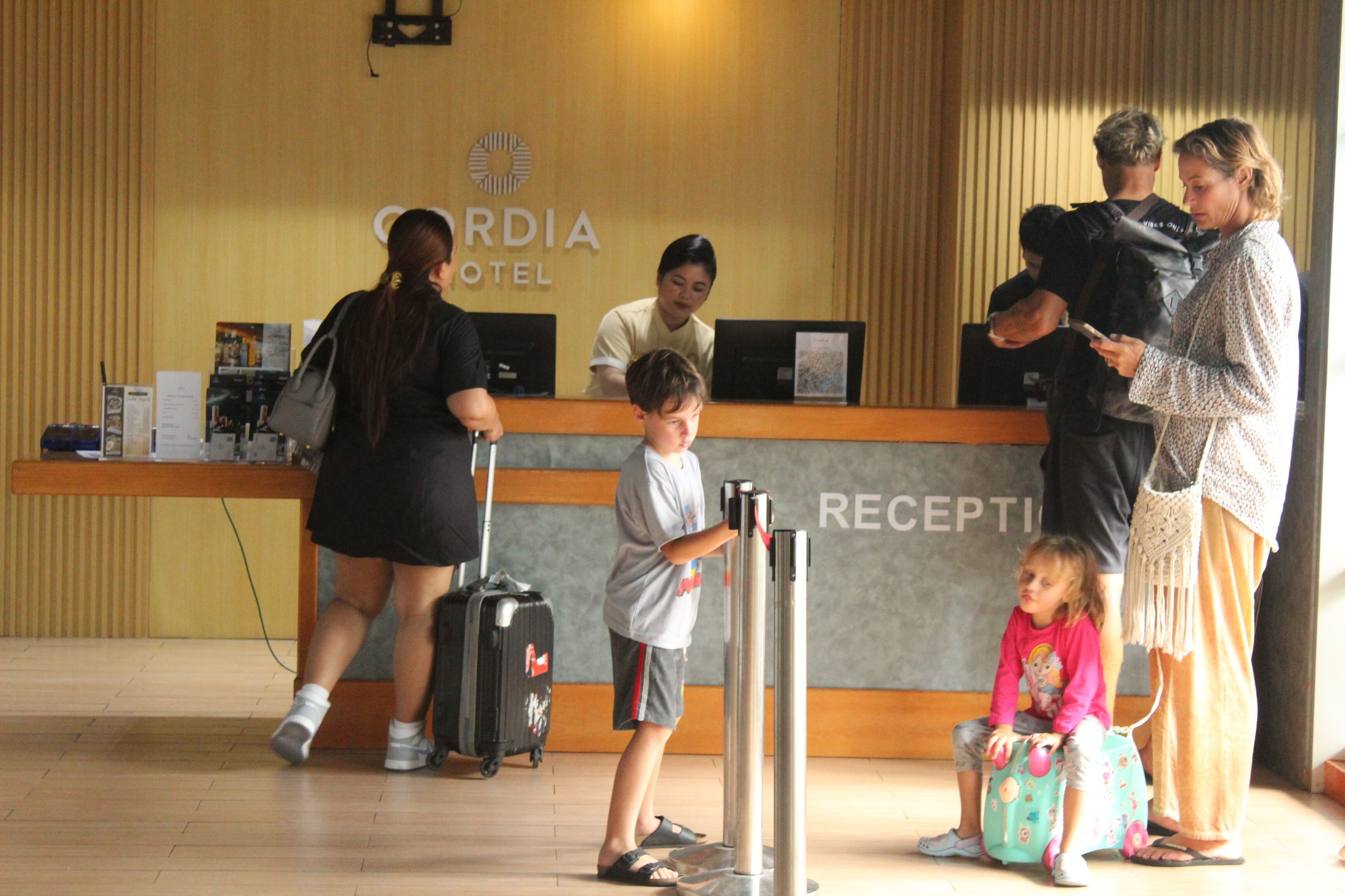 A hotel reception area with a reception desk, a child with a suitcase, and several adults.
