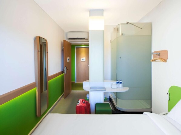 Habitación de hotel con una cama, un escritorio con una computadora portátil, ducha y maleta.