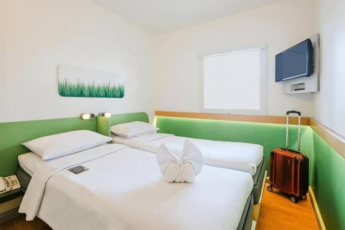 A hotel room with two beds, a green headboard, a television, and a suitcase.