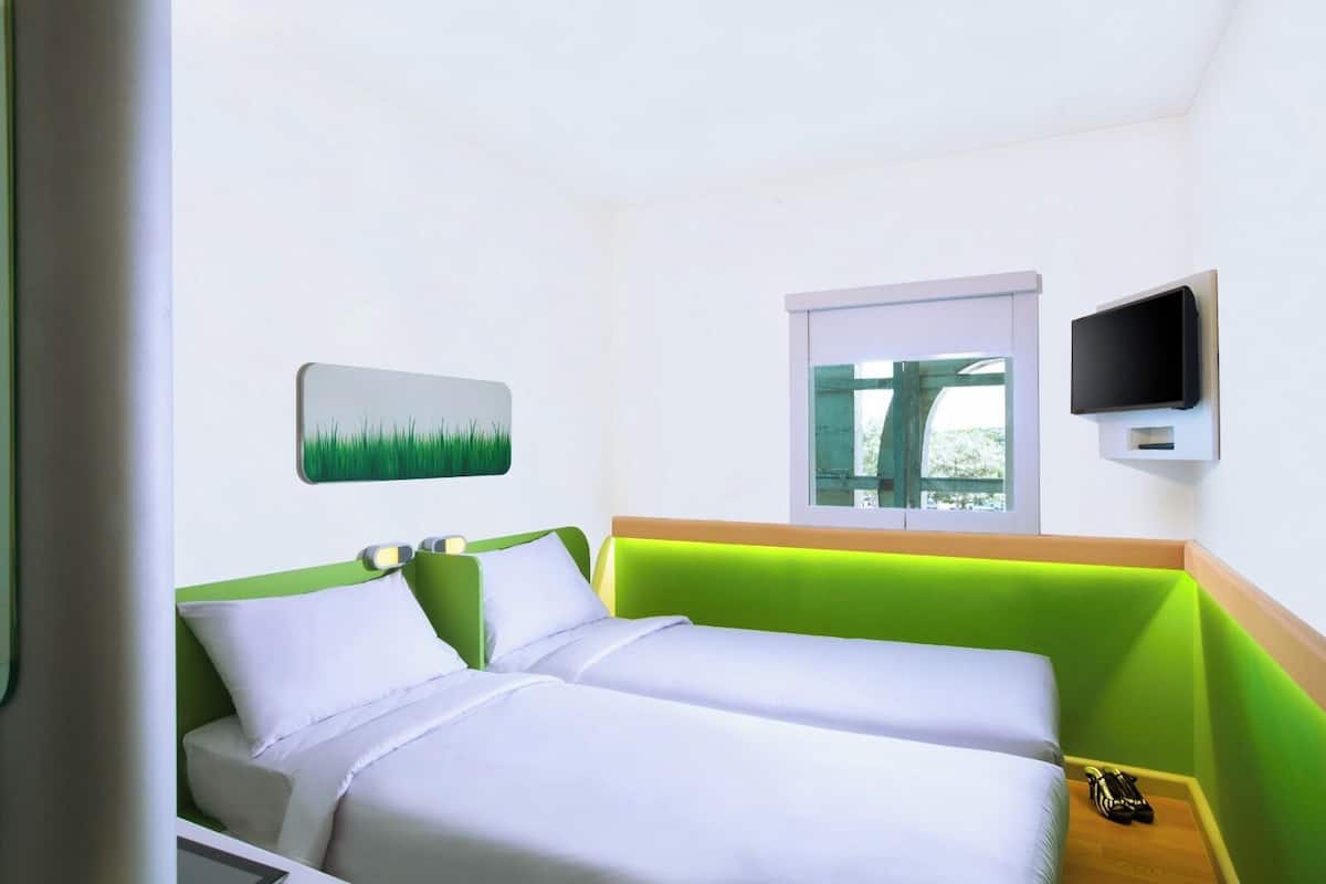 A hotel room with two beds, a TV, a window, and a painting of grass.
