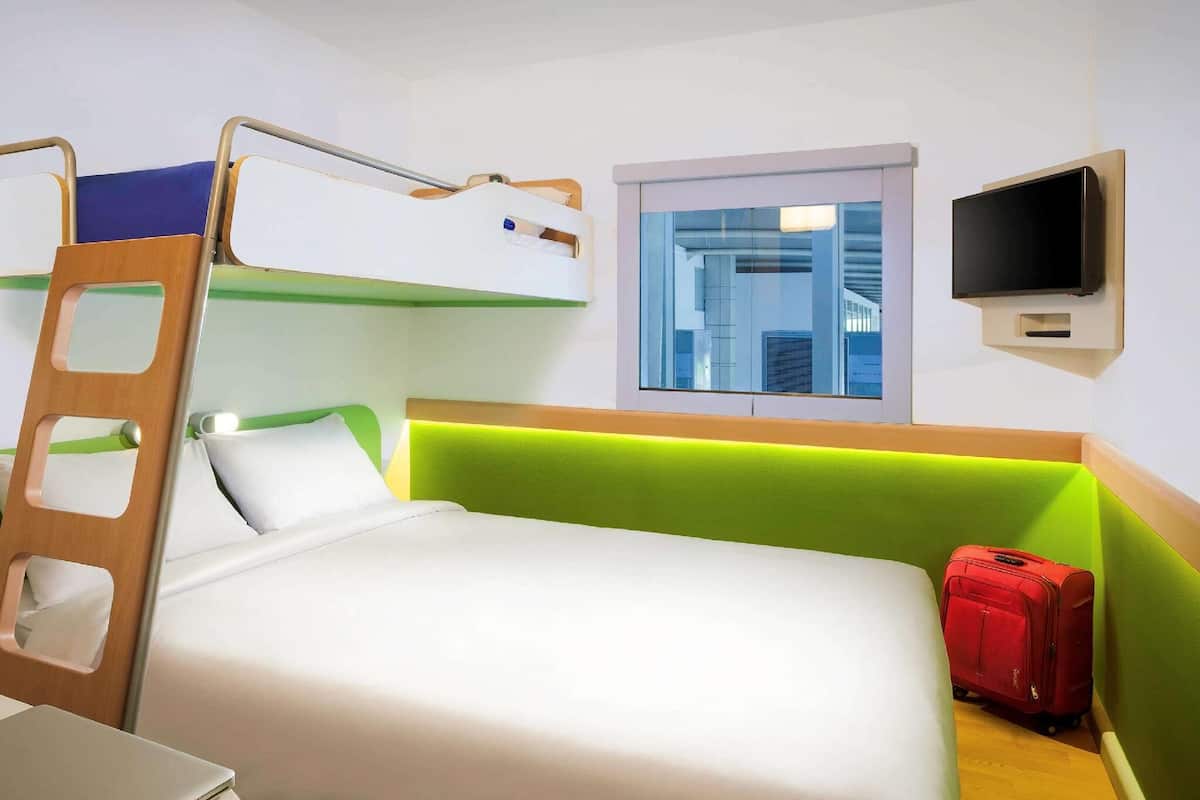 A hotel room with a bunk bed, a desk, a television, and a suitcase.