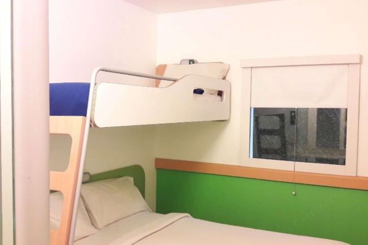 Een slaapkamer met een stapelbed, een raam, een groene wand en een wit hoofdeinde.