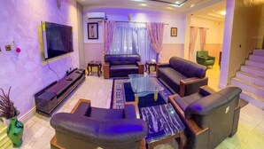 A modern living room with a flat-screen TV, leather sofas, a coffee table, and a staircase leading to an upper level. - House - Sleeps 6 & private parking (Ikeja GRA)