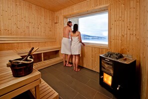 Uma sala de sauna de madeira com uma janela grande, um forno para sauna e um banco de madeira.