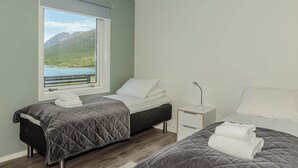 A bedroom with two beds, a window with a mountain view, and a bedside table with a lamp.