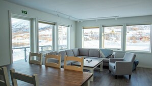 A room with a wooden table, two chairs, a grey sofa, and a window with a snowy view.