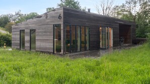 Une maison moderne en bois, dotée de grandes portes-fenêtres coulissantes, d’un espace extérieur couvert et d’un jardin verdoyant.