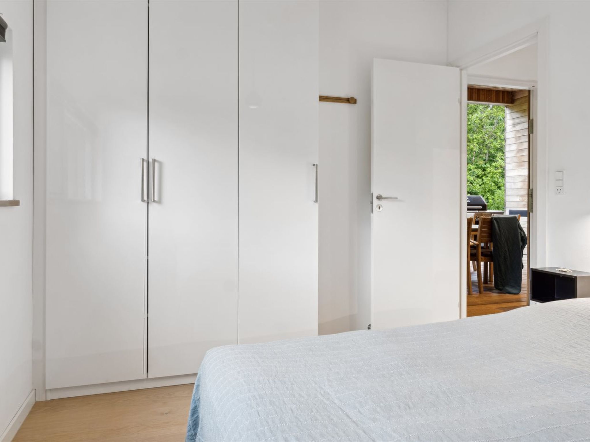 A bedroom with a bed, a wardrobe, and a door leading to an outdoor area with a table and chairs.