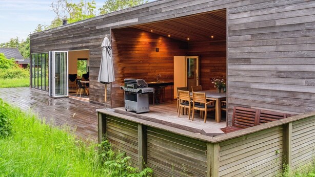 Une cabane moderne en bois dotée d’un patio ouvert, d’un barbecue et d’un coin repas.
