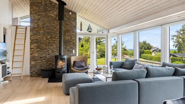 Ein modernes Wohnzimmer mit Kamin aus Stein, grauen Sofas und großen Fenstern mit Blick ins Freie.