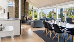 Eine moderne Küche mit Kamin aus Stein, einem Essbereich mit großem Tisch und Stühlen sowie einer gemütlichen Sitzecke mit Sofa und Kissen.