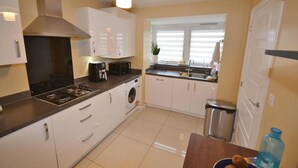 A modern kitchen with white cabinets, a stove, a sink, and a window with blinds.