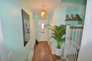 A hallway with a wooden floor, a white door, a hanging light fixture, and a potted plant. - 4 Bed House - Sleeps 8 - Hottub - Garden - Parking (Milton Keynes)