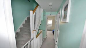 A narrow hallway with a carpeted staircase, light green walls, and a white door at the end.