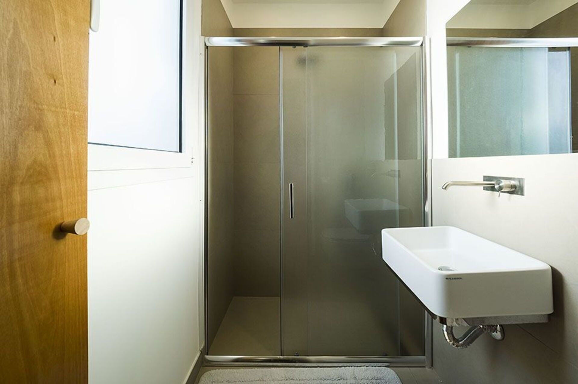 A modern bathroom with a glass shower enclosure, a white sink, and a mirror.
