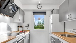 A compact kitchen with white cabinets, a wooden countertop, a stainless steel sink, and a window with a view of greenery.
