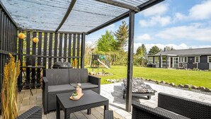 A covered patio with wicker furniture, a grill, and a view of a house and garden.