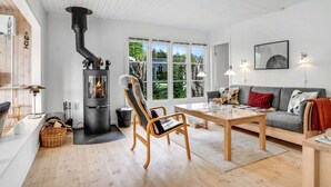 A modern living room with a wood-burning stove, a sofa, a dining table, and a large window.