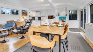 Ett modernt kök med vita skåp, en matplats med ett träbord och stolar samt ett stort fönster med utsikt över omgivningen.