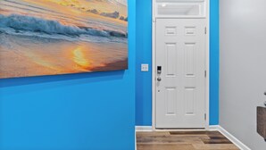 A hallway with a blue wall, a white door, and a painting of a sunset over the ocean. - Stylish & Central Townhome in the Heart of Raleigh (Raleigh)