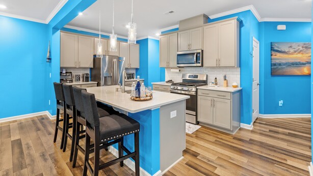 A modern kitchen with blue walls, wooden flooring, and a central island with bar stools. - Stylish & Central Townhome in the Heart of Raleigh (Raleigh)
