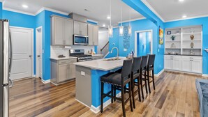 A modern kitchen with a central island, grey cabinets, and a blue accent wall. - Stylish & Central Townhome in the Heart of Raleigh (Raleigh)